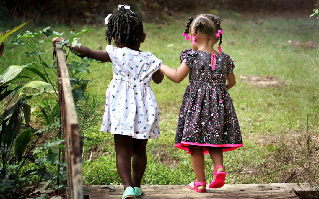 Picture of two young girls holding hands and walking towards a field of grass